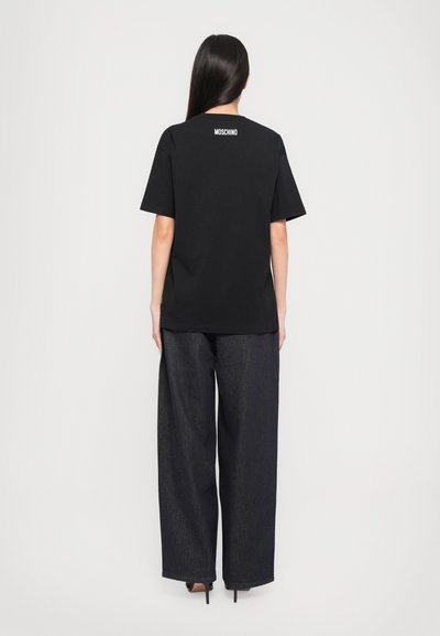 Svart bomullst-skjorte med avslappet passform, med korte ermer og "MOSCHINO"-logo i hvitt på ryggen, sammen med vide denim-bukser.