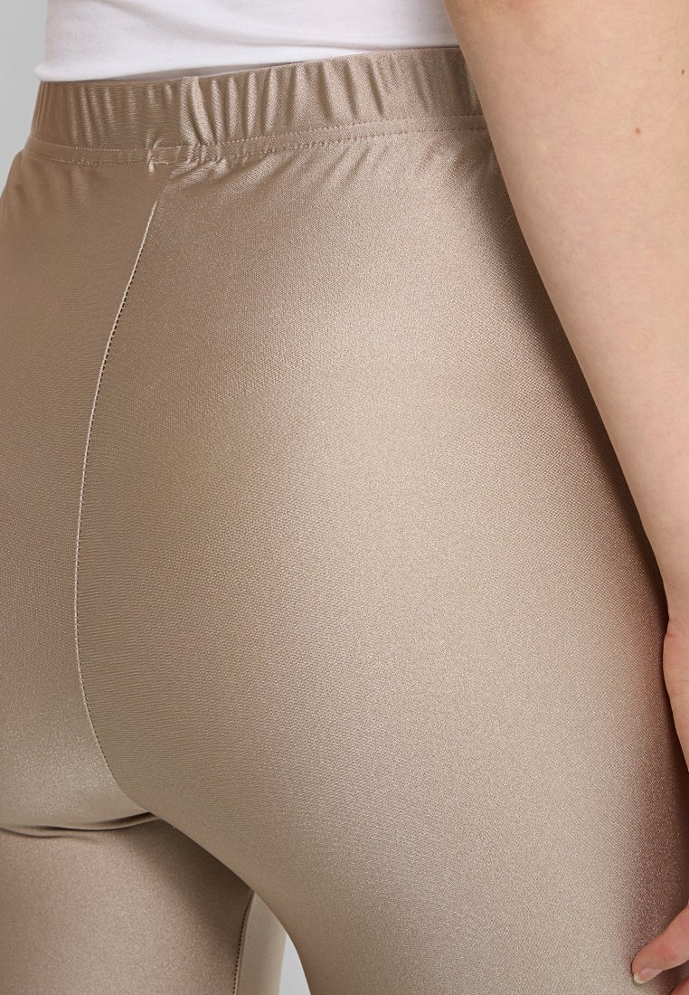 Beżowe elastyczne legginsy o gładkiej, błyszczącej fakturze i elastycznym pasie, z dopasowanym krojem, który podkreśla sylwetkę.