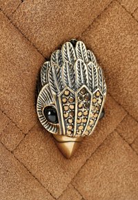 Hardware decorativo in bronzo con design a forma di piuma, dettagli in gemme nere, montato su una superficie in suede marrone testurizzato con un motivo a spina di pesce.