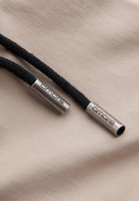 Deux extrémités de cordon tressées noires avec des embouts en métal argenté gravés « ombre » reposant sur un tissu beige.