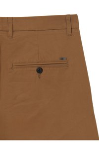 Pantalons marron en tissu lisse présentant une poche arrière unique avec bouton et une petite étiquette de marque en métal.