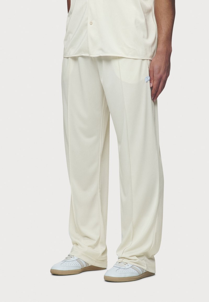 Crema-farbene Polyesterhose mit lockerer Passform, ausgestattet mit einem Logo-Patch auf der rechten Seite und einem glatten, strukturierten Stoff.