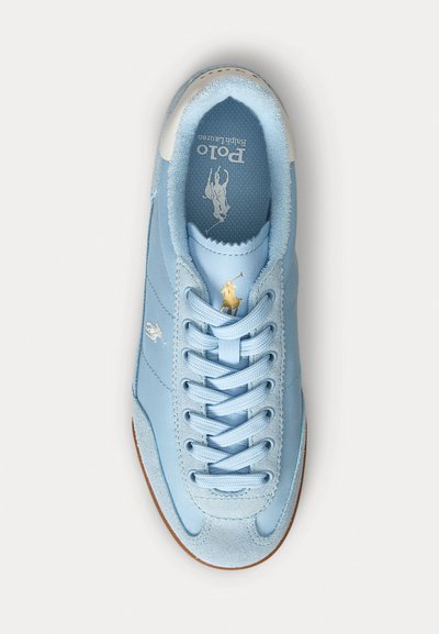 Sapatilha azul clara com material em camurça e têxtil. Apresenta um design com atacadores, sola em borracha e detalhe em logo dourado no linguete e na lateral.