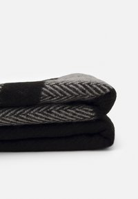 Couverture en laine noire et grise pliée avec un motif en chevrons sur la couche supérieure, présentée sur un fond blanc uni.