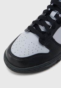 Μαύρο και άσπρο αθλητικό παπούτσι με υφή πάνω από δέρμα, διάτρητη μύτη και επίπεδα μαύρα κορδόνια, με λείο καουτσούκ πάτο.