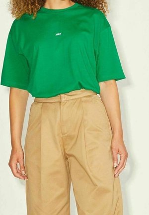 Grünes übergroßes T-Shirt mit kurzen Ärmeln und Rundhalsausschnitt, versehen mit einem kleinen weißen Logo. Kombiniert mit beige-farbenen, hochgeschnittenen Hosen mit weitem Bein.