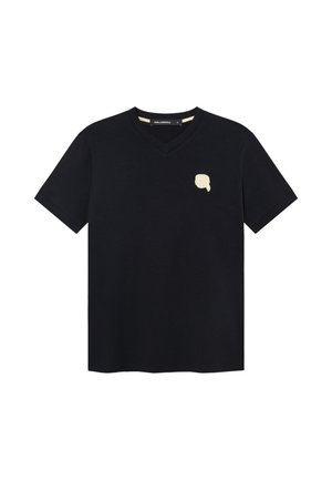 T-shirt noir à col en V et manches courtes, avec un petit motif abstrait beige en forme de visage sur le côté gauche de la poitrine et une étiquette à l'intérieur du col.