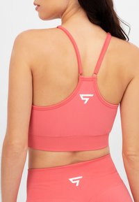 Reggiseno sportivo rosa con spalline regolabili e design aderente. Presenta un dettaglio con logo bianco sul retro e un tessuto liscio ed elastico.