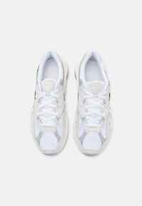 Biała sportowa tenisówka z cholewką z siateczki i zamszu, zaokrąglonym noskiem oraz wyściełanym językiem. Akcenty w jasnoszarym i czarnym kolorze oraz grube białe sznurowadła.