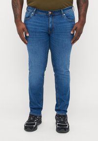 Blå denimjeans med slim fit, med glidelås, fem lommer og kontrasterende søm. Kombinert med svarte joggesko.