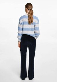 Prúžkovaný pletený sveter v svetlom odtieni modrej a šedej; tmavomodré rozšírené nohavice s cargo vreckami; hladká textúra, priliehavý strih a rebrované manžety.