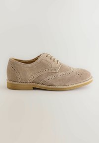 Chaussure oxford en daim beige avec des détails brogues, bout rond et semelle en caoutchouc plate. Présente des œillets pour les lacets et une texture lisse.