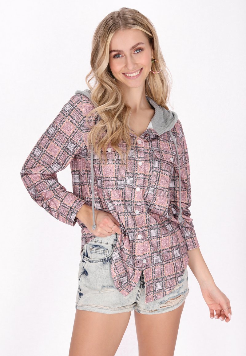 Camicia con bottoni in a fantasia plaid rosa con cappuccio grigio, maniche lunghe e coulisse regolabili. Indossata con pantaloni corti in denim chiaro.
