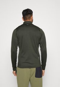 Dark green long-sleeve pullover with a high collar, made of smooth fabric. Features a zippered pocket on the side and a fitted design.