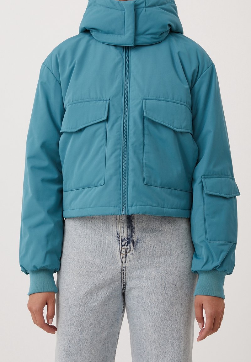 Tealowa krótka kurtka puchowa z kapturem, z zamkiem błyskawicznym z przodu, dwoma kieszeniami na piersi oraz ściagaczami przy mankietach. Gładka, lekka faktura materiału.