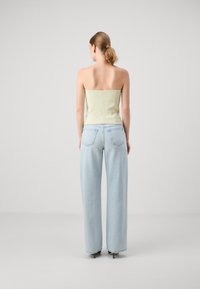 Top sans bretelles vert clair avec un corsage ajusté, associé à un pantalon en jean bleu clair à taille haute et jambes larges. Texture lisse, détails minimalistes.