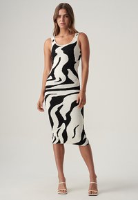 Gestreiftes, schwarz-weißes Strickkleid mit taillierter Silhouette, ärmellosem Design und geripptem Material, das bis zur Mitte der Wade reicht.