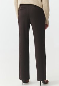 Bruine, hoge taille, rechte broek gemaakt van zachte stof. Bevat achterzakken, strakke lijnen en een gladde textuur. Draagt met zwarte hakken.