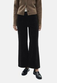 Black wide-leg corduroy pants with a soft texture, featured side pockets, and a high waist. Worn with a brown cardigan and loafers.