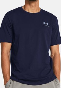 Mörkblå bomullströja med rund hals, korta ärmar och en diskret ljusgrå Under Armour-logga på vänster bröst.