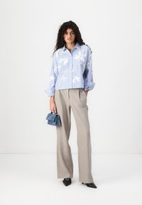 Blusa a righe blu e bianche con stampa floreale, abbinata a pantaloni beige a gamba larga e una borsa blu. Le scarpe nere con punta appuntita completano il look.