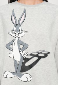 Harmaa huppari, jossa on mustavalkoinen Bugs Bunny -grafiikka, jossa on brodeerattuja yksityiskohtia ja hahmon taustalla varjostusvaikutus.