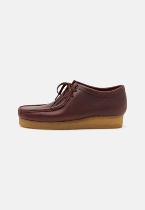Chaussure en cuir brun avec un bout rond, à laçage sur le devant et une semelle en caoutchouc texturée. Présente un design surpiqué le long du bord supérieur.