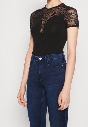 Czarny body z przezroczystym koronkowym karczkiem i krótkimi rękawami, zestawiony z wysokim stanem ciemnoniebieskich jeansów. Gładka tkanina z detalami wzoru koronki.