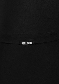 Schwarzer dehnbarer Stoff mit glatter Textur, der einen gestickten Saum und ein kleines Etikett mit der Aufschrift "SMILODOX" aufweist. Keine ausgeprägten Muster oder Akzente.