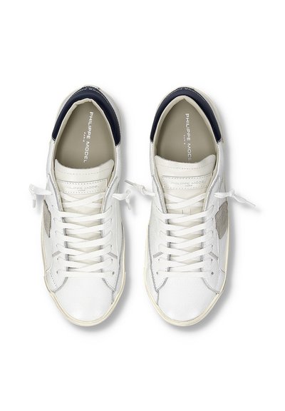 Een paar witte sneakers met lage schoenhoogte, marineblauwe hielaccenten, witte veters en Philippe Model-logo's aan de binnenkant en op de tong.