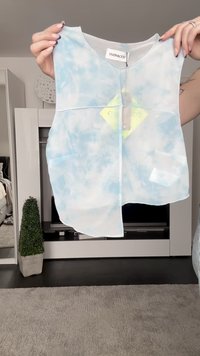 Kerge, varrukateta pluus õhukeses kangas, millel on sinine tükeldatud muster. Ümmargune kaelus, ees lukuga ja taskudetail.