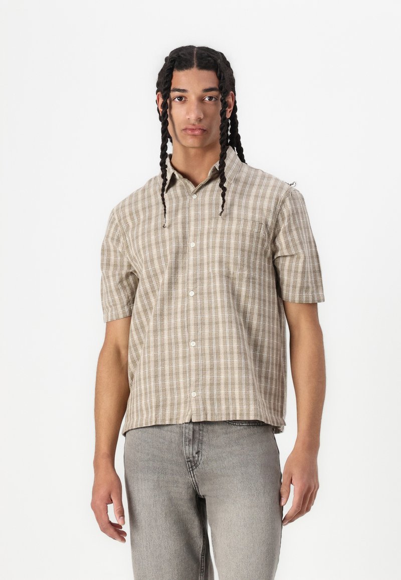 Camicia a maniche corte a quadri nei toni beige e crema, con chiusura a bottoni, taschino sul petto e un design a vestibilità comoda.
