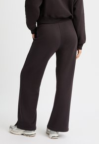 Pantalones de chándal negros de pierna ancha, elaborados con una tela suave y de textura lisa. Con una cinturilla alta y una sutil abertura lateral en el dobladillo.