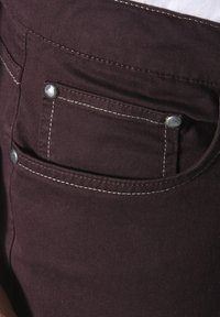 Burgundy denim pants with visible silver hardware, contrasting white stitching, and a front pocket detail. Smooth texture.