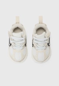 Baskets en maille blanches avec des accents beiges, logo noir sur le côté et lacets plats. Elles possèdent une petite languette au talon pour un enfilage facile.