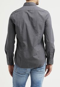 Harmaa pitkähihainen paita, jossa on teksturoitu kuvio, napillinen kaulus ja kalvosimet. Yhdistetty vaaleansinisien suoraleikkaisten farkkujen kanssa.