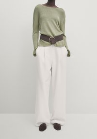 Green knit sweater with long sleeves, paired with white high-waisted trousers and a brown leather belt featuring a brass circular buckle.