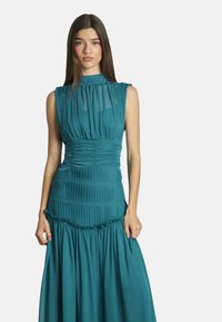 Türkises, ärmelloses Kleid mit gerafftem Oberteil und ausgestelltem, gestuftem Rock. Verfügt über einen hohen Kragen und einen strukturierten Stoff mit Falten.