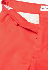 Pantalones de algodón rojos con una textura suave y costuras visibles. Presentan una cinturilla con cierre de gancho y una etiqueta de tela cerca de la parte superior.