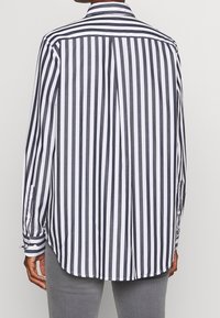 Långärmad skjorta med svartvita vertikala ränder, knappmanchetter och standardkrage. Har en avslappnad passform och en böjd nederkant.