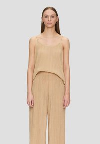 Beige geplooide mouwloze top met een ontspannen pasvorm, delicate bandjes en een zachte textuur. Gepaard met bijpassende losse broek.
