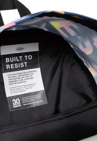 Interior negro de una mochila con una textura suave, con una etiqueta que dice "Construido para Resistir" en letras blancas en negrita sobre un fondo multicolor.