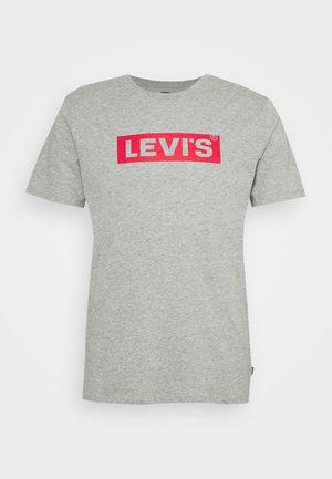 T-shirt gris en coton avec un col ras du cou. Présente un logo rectangulaire rouge bien visible avec "LEVI'S" en texte blanc. Manches courtes.