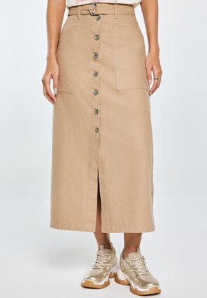 Beige midi sukně vyrobená z bavlny s detailem předních knoflíků, dvěma náprsními kapsami a předním rozparkem. V kombinaci se zlatými sportovními teniskami.