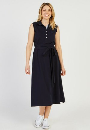 Robe sans manches bleu marine avec col, patte de boutonnage et taille nouée. Fabriquée dans un tissu doux, elle est de longueur midi et se marie avec des baskets blanches.
