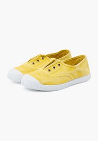 Zapatillas amarillas de lona tipo slip-on con suelas de goma blanca y ojales, que presentan una textura suave y un diseño de punta redonda.