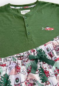 Grön bomullstop med knapplist och broderad röd bil. Kjolen har ett festligt tryck av figurer och träd, samlad med en grön rosett.