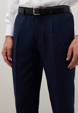 Marine-kariertes Tuchhose aus strukturiertem Stoff, mit einem schwarzen Ledergürtel und einer silbernen Schnalle, sowie einem sichtbaren weißen Hemdkragen.