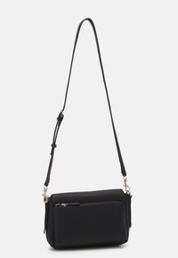 Sort crossbody taske lavet af tekstureret materiale, med en lynlåslomme, justerbar rem og hardware i guldtoner. Firkantet form.