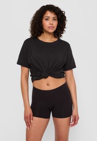 Svart bomullströja med knuten front och korta ärmar, kombinerad med högmidjade svarta shorts. Slät textur, åtsittande design.